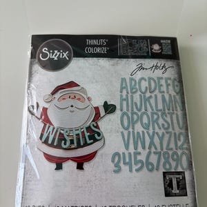 May include: A Sizzix Thinlits Colorize die set featuring a Santa Claus design with the word "Wishes". The set includes letters, numbers, and various shapes. The packaging has the text "Jim Holtz" and "49 Dies".
