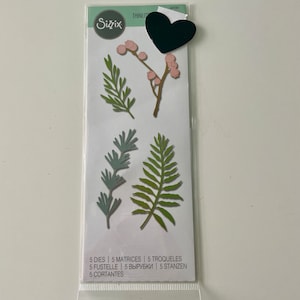 May include: A package of five die-cut metal stencils for crafting. The stencils feature various leaf and berry designs in shades of green, pink, and brown. The package includes the text "5 DIES | 5 MATRICES | 5 TROQUELES 5 FUSTELLE | 5 ВЫРУБКИ | 5 STANZEN 5 CORTANTES".