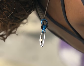 Collar con mosquetón azul en forma de ocho y cuerda negra para escalar.