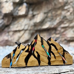 May include: Wooden mountain-shaped display with climbing gear accents. The display features a natural wood grain finish with dark brown accents. Colorful climbing cams are attached, adding a vibrant touch to the piece. A unique decorative item.