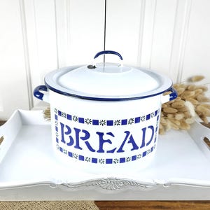 May include: White enamel bread bin with a lid, blue trim, and handles. The word "BREAD" is displayed in blue lettering with a floral pattern. The bin sits on a white tray with handles.