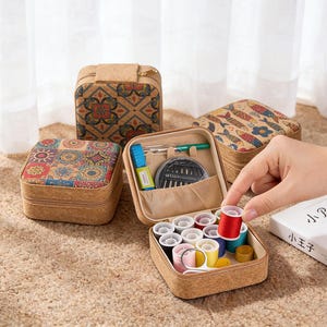 Può includere: Kit da cucito in sughero con una varietà di rocchetti di filo colorati, aghi e piccole forbici. Il kit ha un coperchio fantasia e una chiusura a zip. Il kit è aperto, rivelando il contenuto.