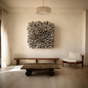May include: A contemporary living room featuring a large, square, grey abstract wall art piece. Below the art is a long, wooden bench and a low, rectangular coffee table. A wooden chair with a white cushion is on the right.