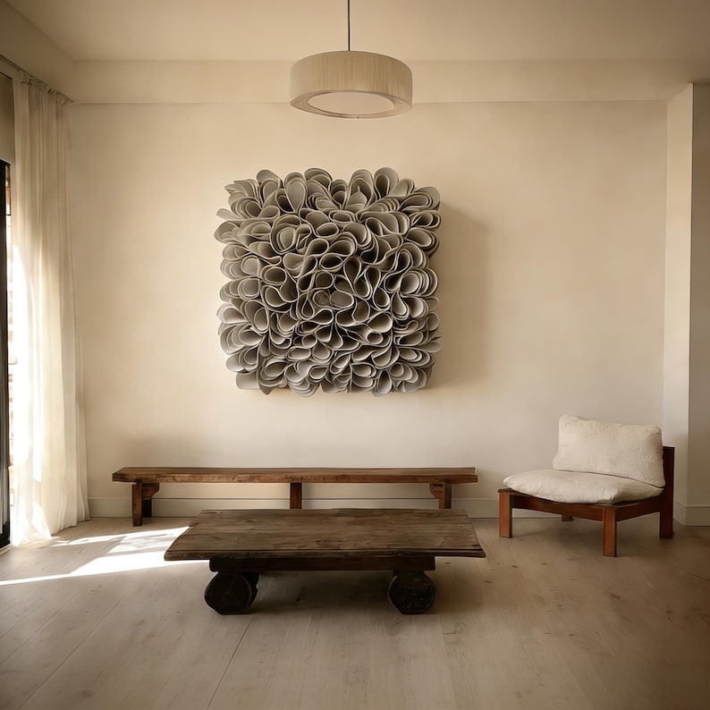 May include: A contemporary living room featuring a large, square, grey abstract wall art piece. Below the art is a long, wooden bench and a low, rectangular coffee table. A wooden chair with a white cushion is on the right.