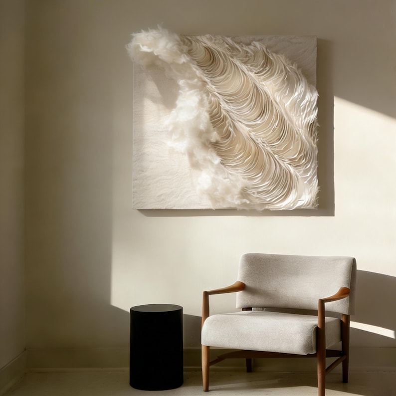 May include: A large, textured, cream-coloured wall art piece with a layered, wave-like design. The artwork hangs above a mid-century modern style chair with a light grey seat and wooden arms. A black cylindrical side table sits to the left of the chair.