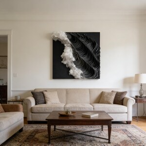 May include: Abstract wall art with a black background and layered, wavy black and white elements. The artwork is mounted above a beige sofa in a bright living room. The room has a rug and a wooden coffee table.