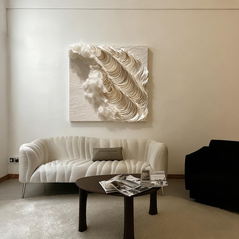 May include: A living room with a white, curved sofa, a dark brown coffee table, and a black armchair. A piece of wall art with a layered, wave-like design hangs above the sofa. The room has a neutral colour palette.