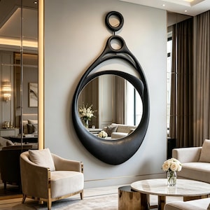 May include: A large, black, organic-shaped wall mirror featuring a smooth, matte frame with a continuous, flowing silhouette. The design includes two circular cutouts at the top, transitioning into a wide, asymmetrical, teardrop-like main frame.
