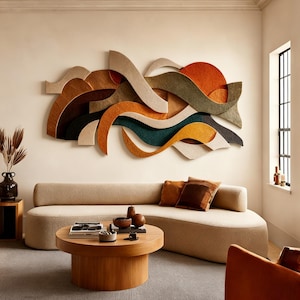May include: A modern living room featuring a beige sofa, a round wooden coffee table, and an abstract wall art piece. The wall art has a layered design with various colors, including brown, orange, green, and yellow. Decorative pillows and a vase with dried plants add to the room's aesthetic.