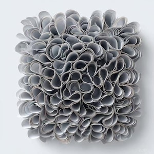 May include: An abstract artwork featuring a square arrangement of numerous grey, curled paper elements. The paper is densely layered, creating a textured, three-dimensional effect. The piece is set against a plain white background, highlighting the form.