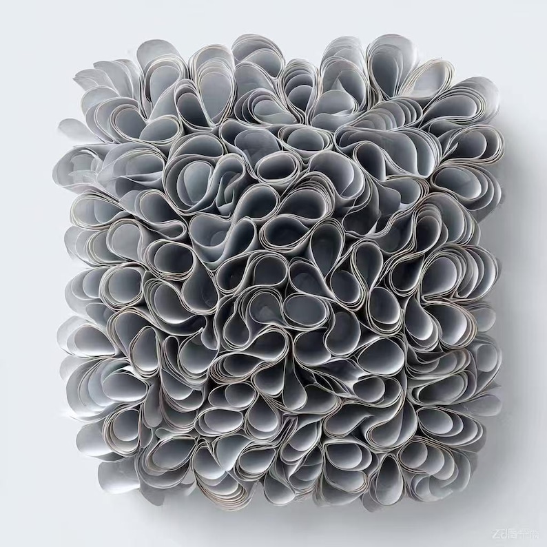 May include: An abstract artwork featuring a square arrangement of numerous grey, curled paper elements. The paper is densely layered, creating a textured, three-dimensional effect. The piece is set against a plain white background, highlighting the form.