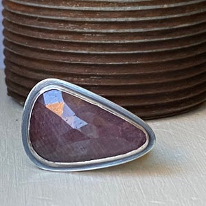 Pode incluir: Um anel de prata com uma grande gema roxa facetada engastada em uma moldura.