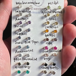 Könnte beinhalten: Eine weiße Karte mit den Namen verschiedener Edelsteine und einer kleinen Probe jedes Steins. Die Steine sind in Reihen angeordnet und mit ihren Namen beschriftet. Die Karte wird in einer Hand gehalten.