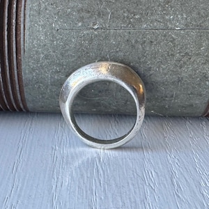May include: A silver ring with a rounded, slightly curved design. The ring is smooth and has a polished finish.