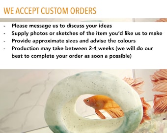 May include: A ceramic aquarium decoration with a circular opening, in shades of white and teal, houses a vibrant orange betta fish. The text "WE ACCEPT CUSTOM ORDERS" is displayed above the aquarium.