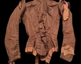 May include: A brown long-sleeved blouse with a high collar and ruched detailing. The blouse has a fitted bodice and a loose, flowing skirt.