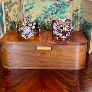May include: Two ornate copper bracelets with clear crystal accents, displayed in a wooden box with a decorative inlay.