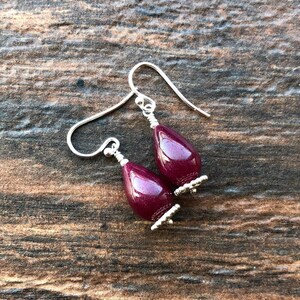 May include: A pair of silver dangle earrings with teardrop-shaped burgundy gemstone beads.
