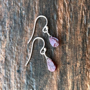 May include: A pair of silver dangle earrings with red gemstone drops. The earrings are on a wooden surface.