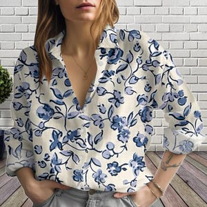 May include: A cream-colored button-down shirt with a blue floral pattern. The long-sleeved shirt features a V-neck and is made of a lightweight fabric. The floral design includes blue flowers and leaves, creating a feminine and stylish look.