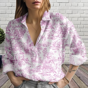 Pode incluir: Camisa branca com estampa toile de Jouy rosa. A camisa de manga comprida apresenta decote em V e um design detalhado de figuras, carruagens e elementos florais. A camisa é feita de tecido leve.