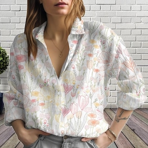 Puede incluir: Camisa blanca con estampado floral con botones y mangas largas. El patrón presenta flores rosas, amarillas y verdes sobre un fondo blanco. La camisa tiene un cuello clásico y es adecuada para el uso diario. El diseño floral es una impresión delicada.