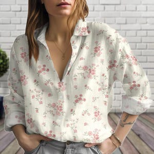 May include: A button-down shirt with a floral pattern. The shirt is off-white with pink roses and green leaves. The long-sleeved shirt has a collar and is unbuttoned at the top.