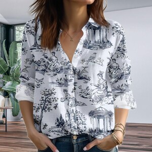May include: White button-down shirt with a blue and white toile pattern. The long-sleeved shirt features a classic design with scenes of figures, trees, and architectural elements. The shirt has a collared neckline and button closures.