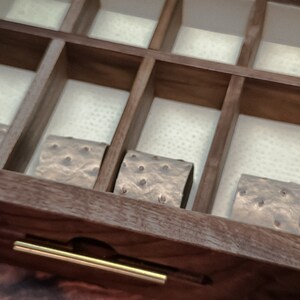 May include: A wooden box with a drawer and a gold handle. The drawer is open and contains four small, square, brown objects with a textured surface.