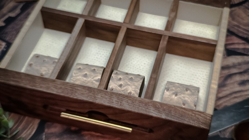 May include: A wooden box with a drawer and a gold handle. The drawer is open and contains four small, square, brown objects with a textured surface.