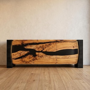 May include: A modern wooden sideboard with a natural wood grain finish and black accents. The cabinet features a unique design with a dark, river-like inlay across the front. The piece is set on black legs and has a curved design.