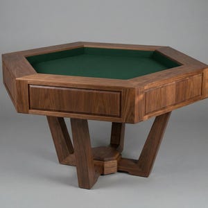 May include: A solid wood, octagonal game table with a green felt playing surface. The table has a drawer and is supported by a unique, angled leg design. The wood has a rich, dark brown finish.