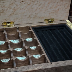 May include: A wooden jewelry box with a hinged lid, featuring a compartment with multiple slots for rings and a separate compartment with a black velvet lining for storing necklaces or bracelets.