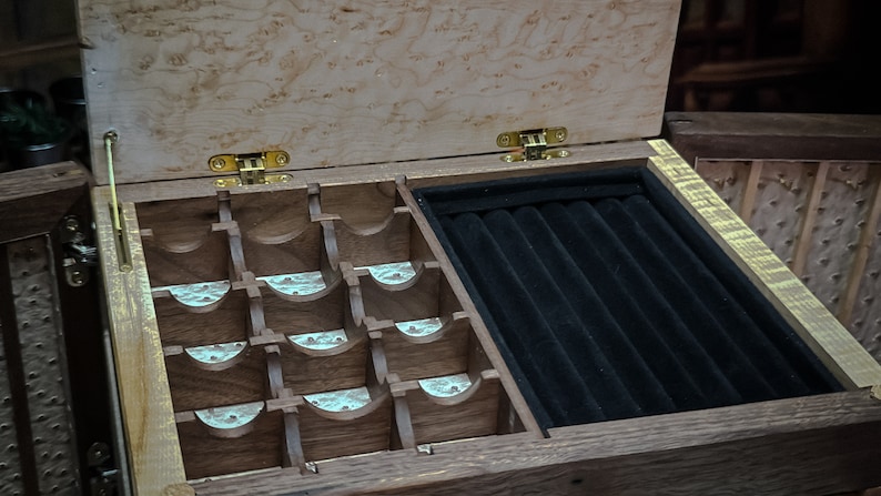 May include: A wooden jewelry box with a hinged lid, featuring a compartment with multiple slots for rings and a separate compartment with a black velvet lining for storing necklaces or bracelets.