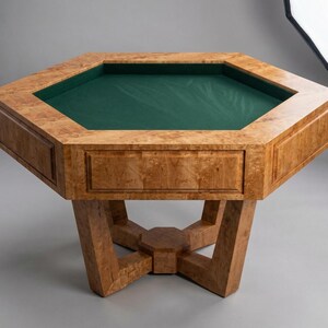 May include: A wooden octagonal poker table with a green felt playing surface. The table has a light brown, burl wood finish and a geometric base. The table is approximately 40 inches wide and 30 inches tall.