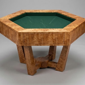 May include: A hexagonal wooden game table with a green felt playing surface. The table has a light brown, burl wood finish and a drawer. The legs are angled and connected by a central support.