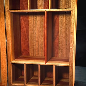 Puede incluir: Una caja de madera con tapa con bisagras y varios compartimentos. La caja está hecha de diferentes tipos de madera, creando un patrón único e intrincado.