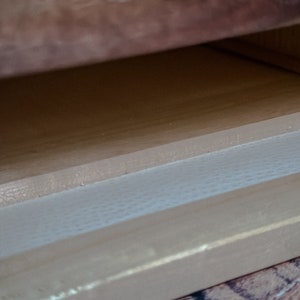May include: Close-up of a wooden drawer with a white liner. The drawer is open and the liner is visible.