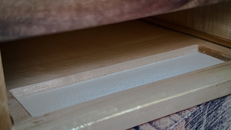 May include: Close-up of a wooden drawer with a white liner. The drawer is open and the liner is visible.