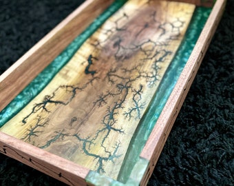 May include: A wooden tray with a green epoxy resin inlay. The wood has a natural wood grain and the resin has a swirling pattern. The tray is perfect for serving snacks or drinks.