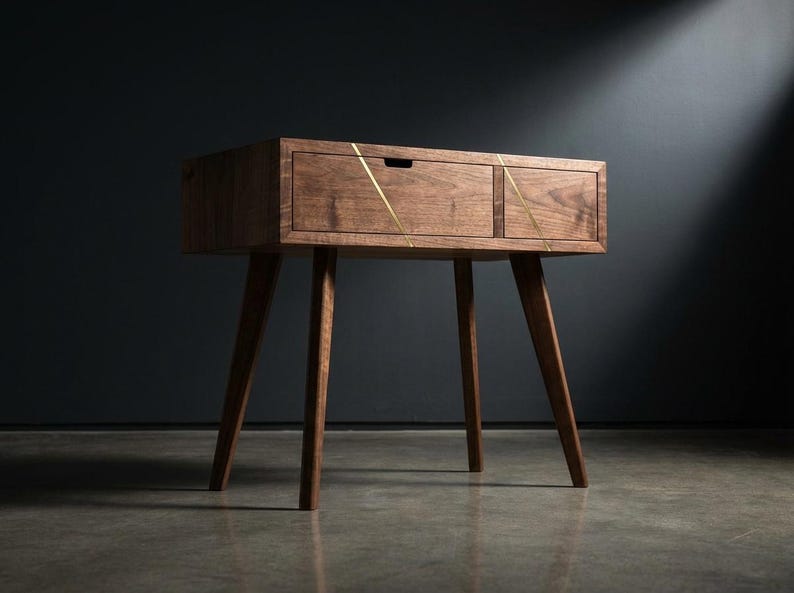 May include: A mid-century modern wooden side table with a drawer and angled legs. The table is made of dark wood and features brass inlay accents. The design is minimalist and the table is suitable for a living room or bedroom.