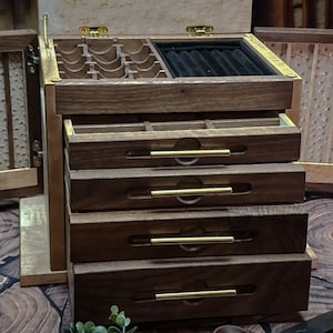 May include: A wooden jewelry box with a hinged lid and multiple drawers. The box is made of dark wood with brass accents. The lid is open and reveals a compartment with a black velvet lining. The box has four drawers with brass handles.
