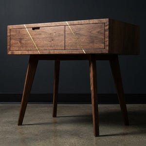 May include: A mid-century modern wooden nightstand with two drawers and angled legs. The nightstand is made of dark wood and features brass accents. The drawers have a simple, minimalist design, and the legs are tapered.