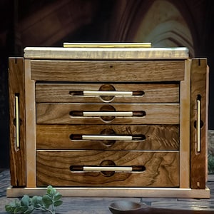 May include: A wooden box with five drawers and brass pulls. The box is made of dark wood with a light wood trim. The box is sitting on a wooden surface.