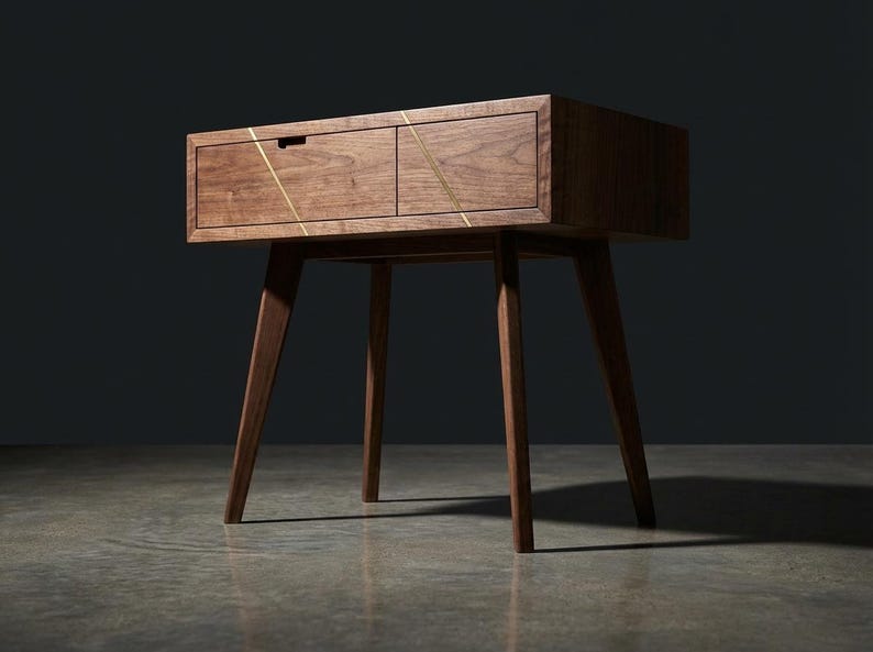 May include: A mid-century modern wooden nightstand with two drawers and angled legs. The nightstand is a warm brown color with gold accent lines across the drawer fronts. The design is minimalist and stylish.