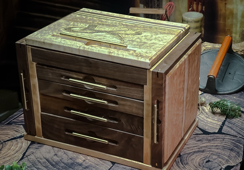 May include: A wooden box with four drawers and brass pulls. The top of the box is made of a light wood with a gold-colored finish. The box is sitting on a wooden surface.