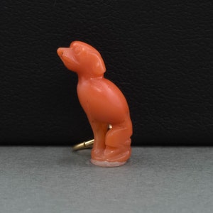 May include: A coral bird figurine with a gold-colored ring attached to its leg. The bird is perched on a base and has a detailed design.