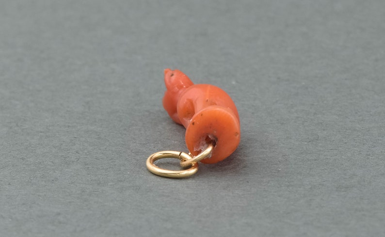 May include: A coral pendant in the shape of a crouching cat with a gold jump ring.