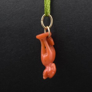 May include: A red coral pendant in the shape of a standing animal, hanging from a gold chain with a green ribbon.