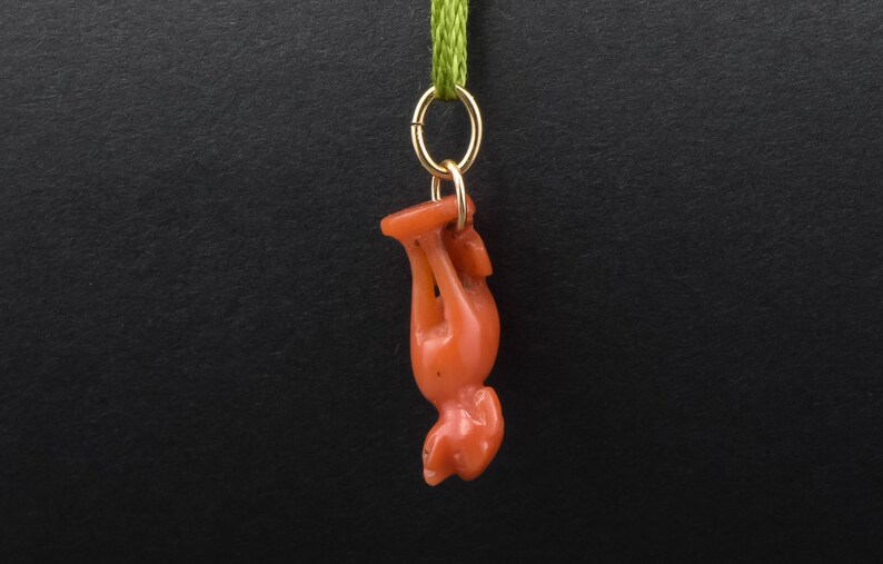 May include: A red coral pendant in the shape of a standing animal, hanging from a gold chain with a green ribbon.